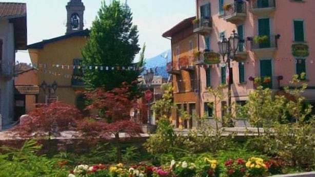A traditional European town square with historic buildings, a church tower, and a well-maintained garden with colorful flowers. - Albergo Centrale (Fino del Monte)