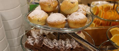 A multi-tiered display of muffins and brownies, with a variety of fruits and pastries in the background.