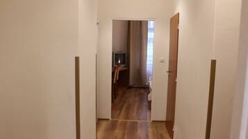 Un estrecho pasillo con piso de madera que conduce a una habitación con cama y televisión.