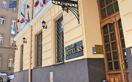 A hotel entrance with a wrought iron canopy, a sign reading "Gallery Hotel SIS," and multiple national flags.