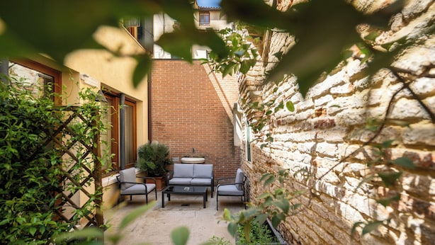 A patio area with a brick wall, a sofa, and two chairs. - Ca' Pozzo Inn (Venice)