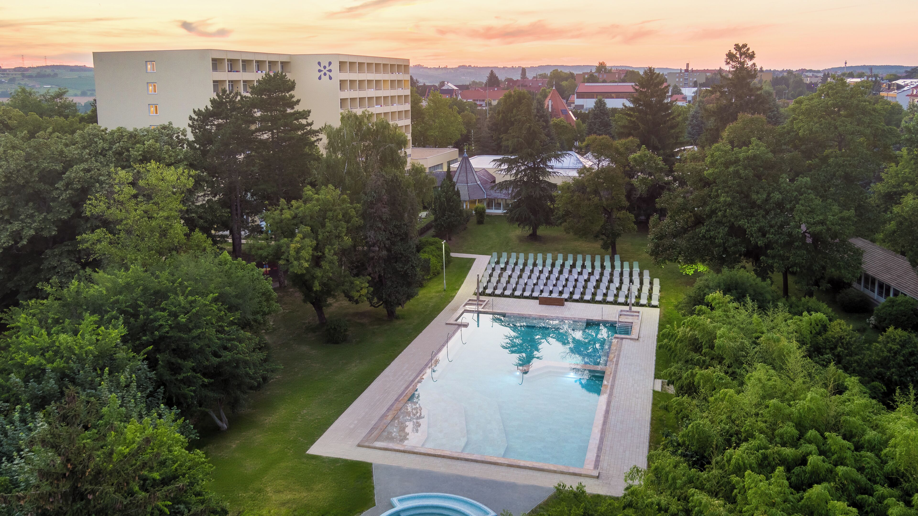 A swimming pool surrounded by lush greenery, with a view of a building in the background.