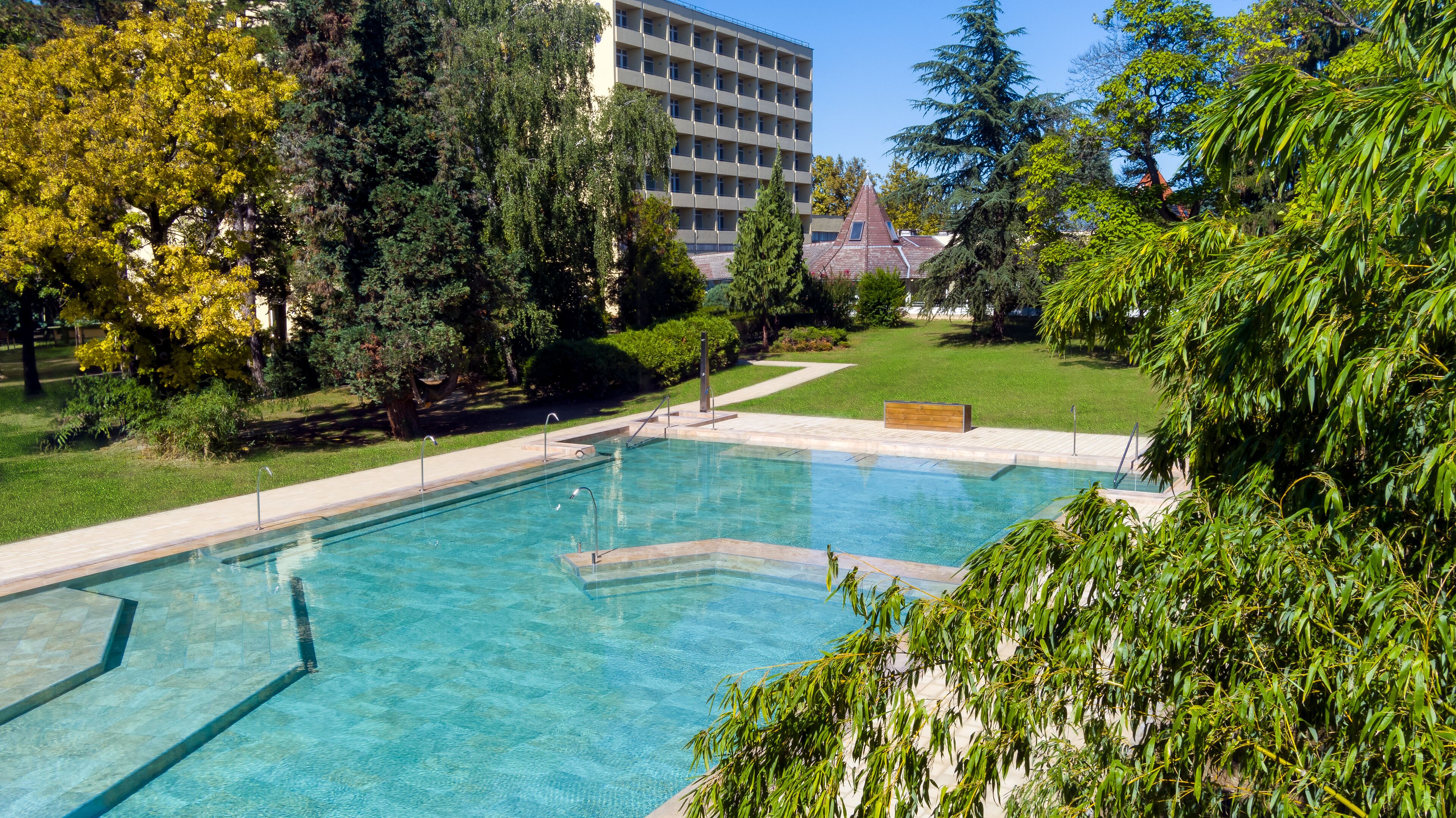 Una piscina rectangular con agua azul cristalina, rodeada por una terraza pavimentada.