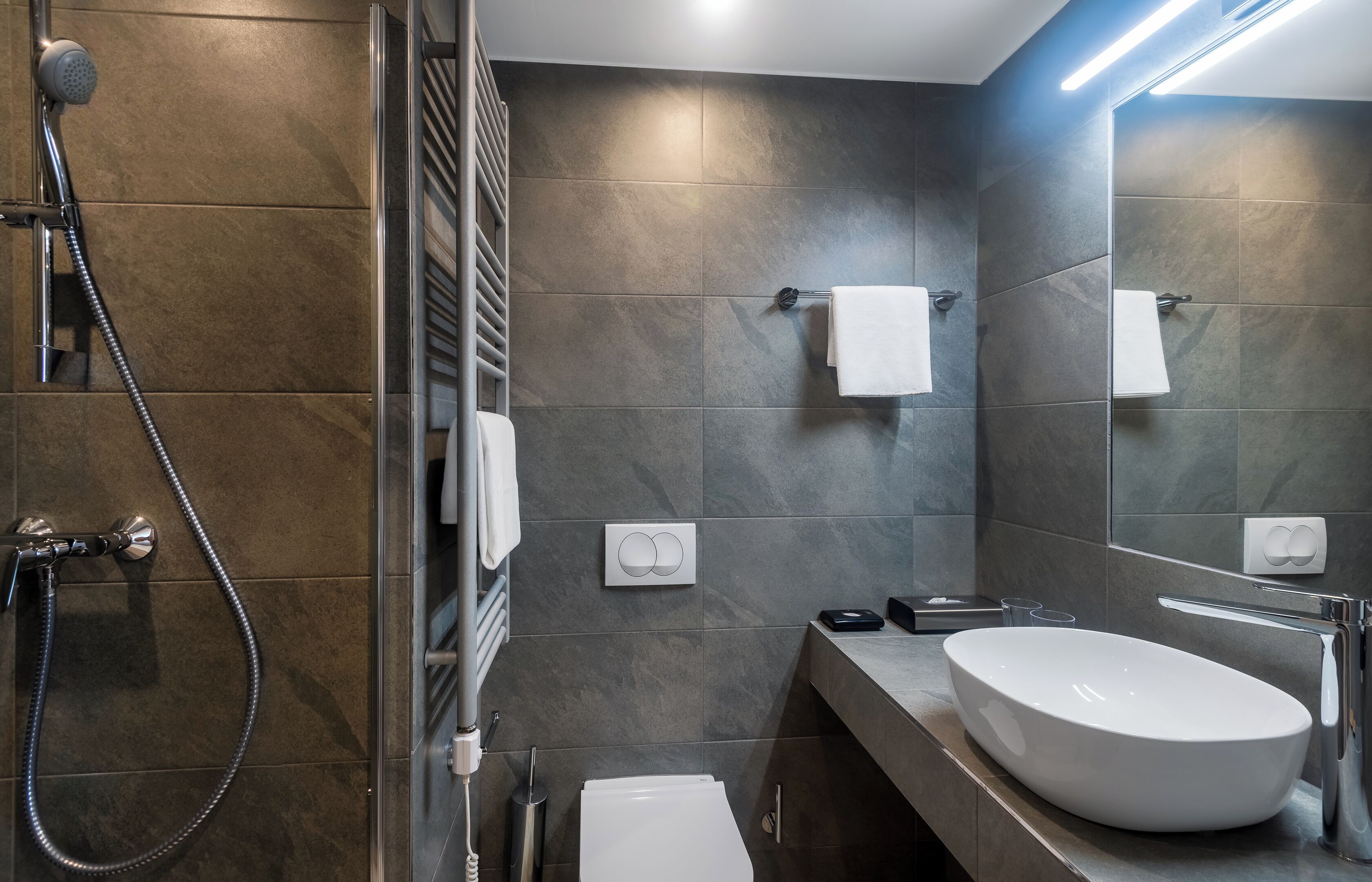 A modern bathroom with a large sink, a shower, and a mirror.