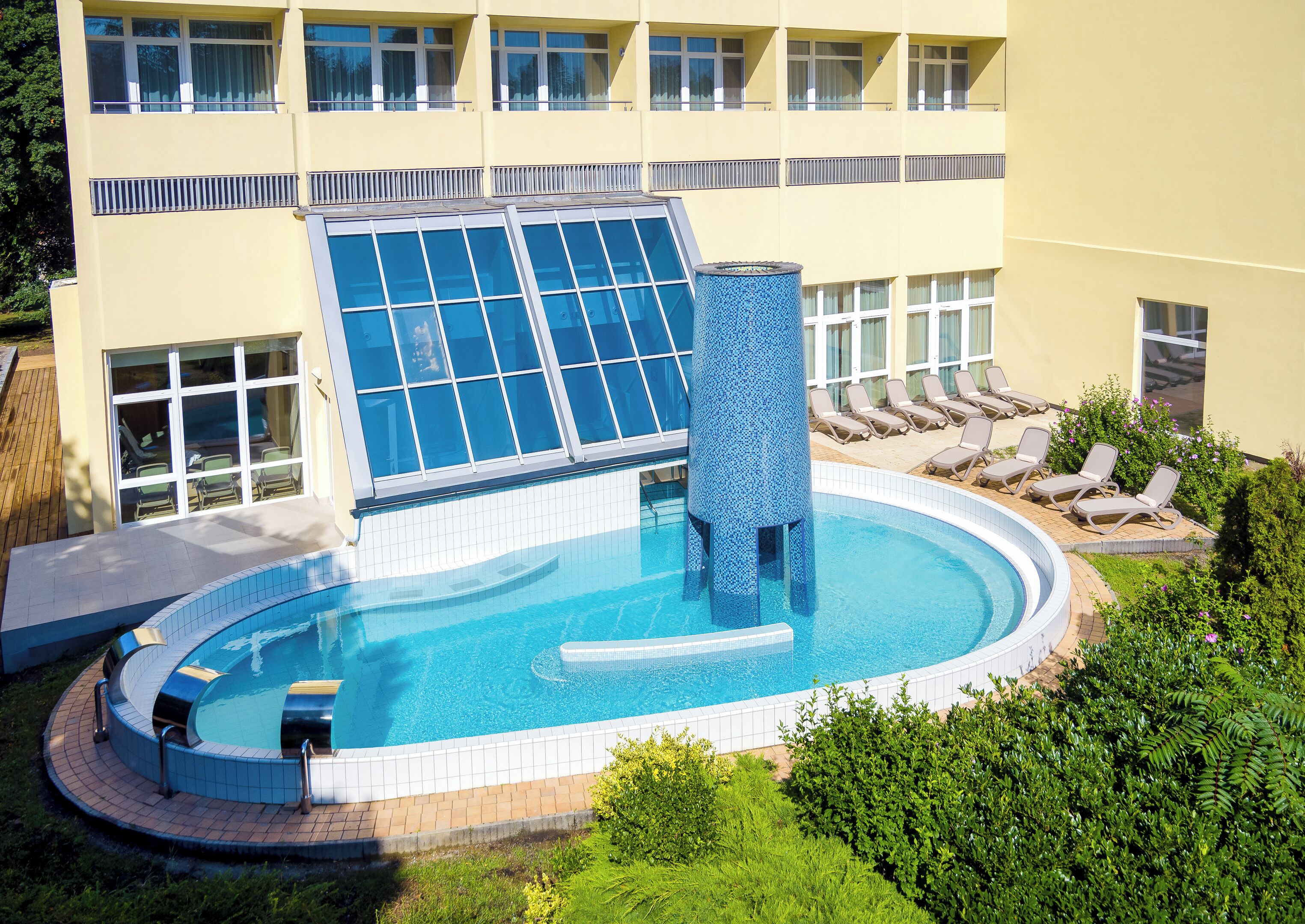 Une piscine dotée d’une structure en verre, d’un élément décoratif aquatique et de chaises longues.