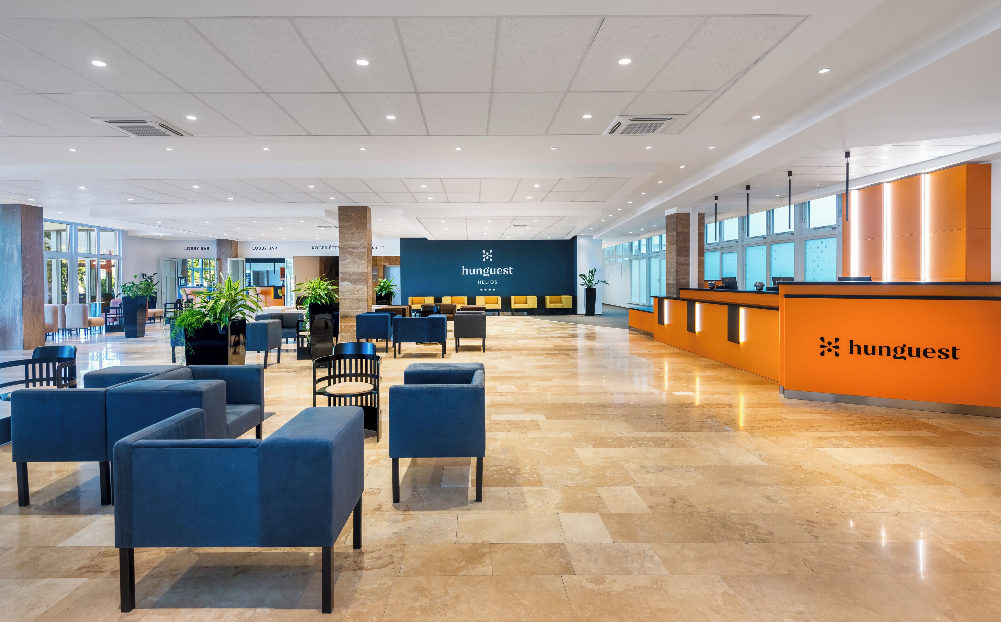 A modern lobby with seating areas, a reception desk, and a large wall displaying the 'hunguest' logo.