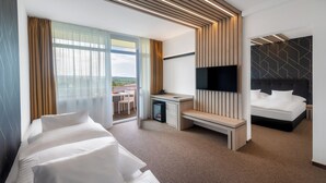 A modern hotel room with a bed, a desk, a TV, and a balcony with a view. - Hunguest Hotel Helios (Hévíz)