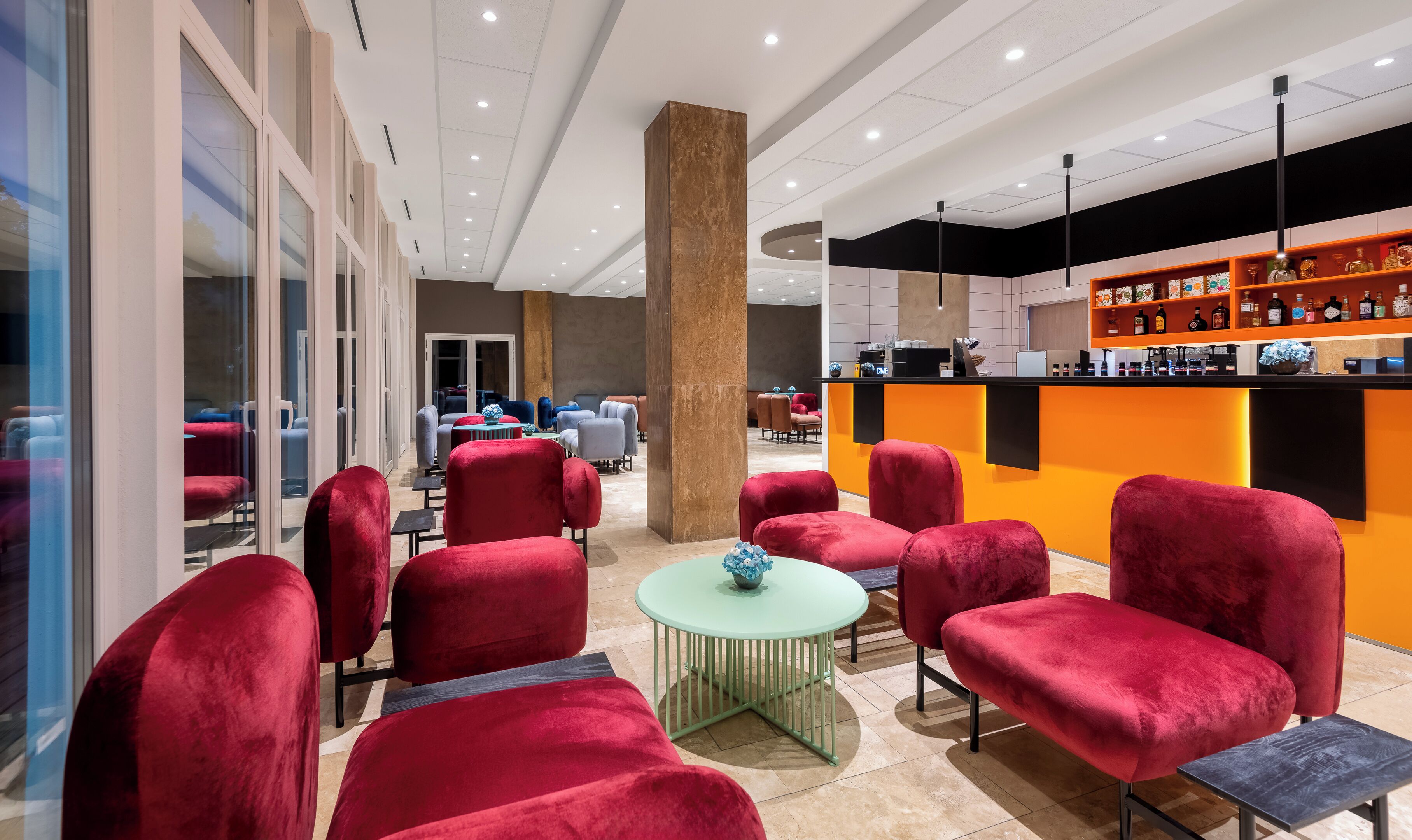 A modern lounge area with red upholstered chairs, a small round table with a vase, and a bar area with shelves of bottles.