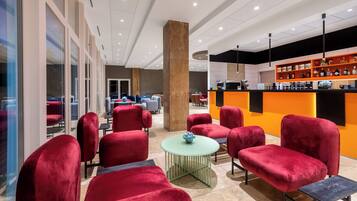 A modern lounge area with red upholstered chairs, a small round table with a vase, and a bar area with shelves of bottles.