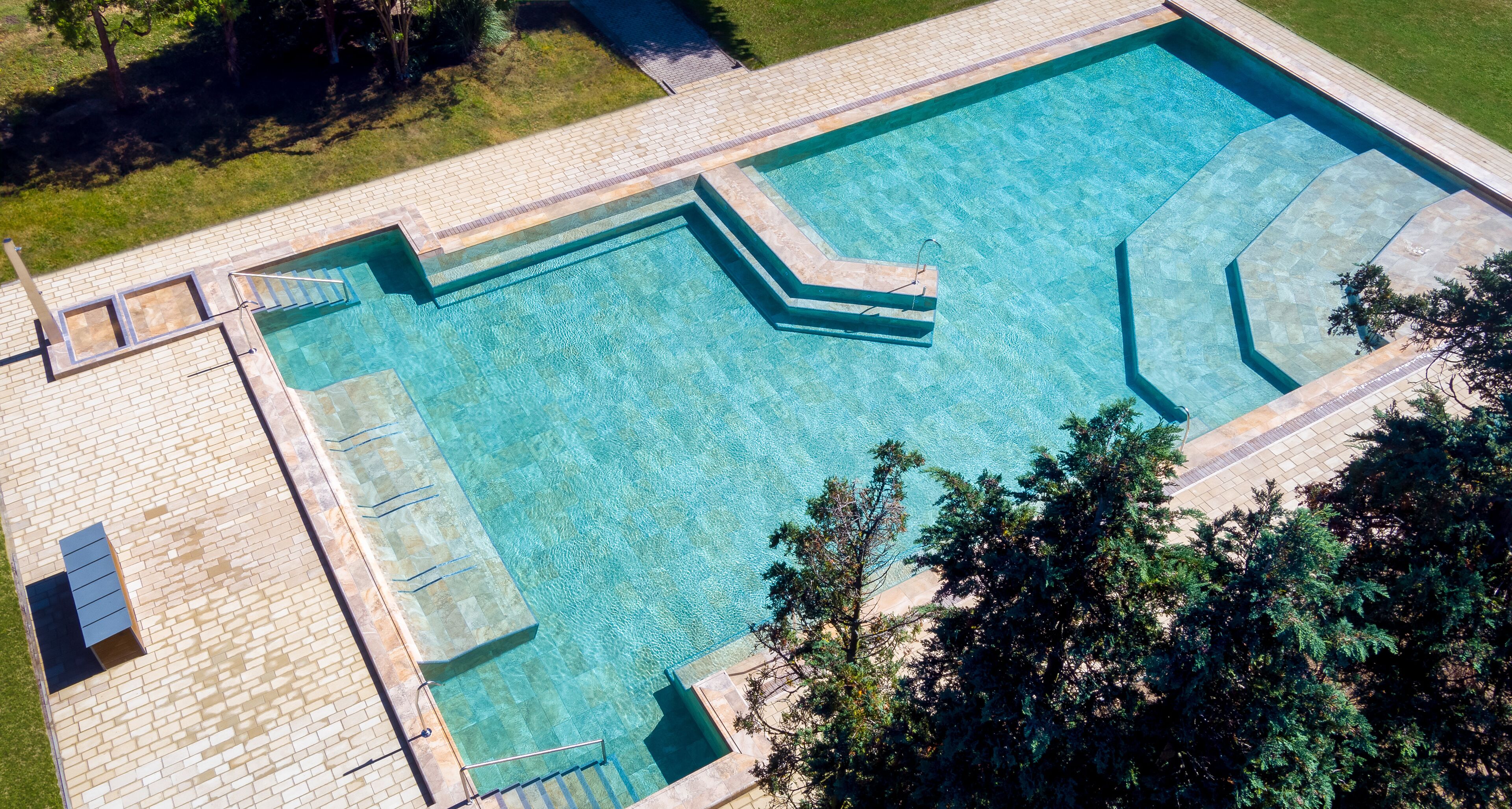 An aerial view of a rectangular swimming pool with a stone border and a small deck area.