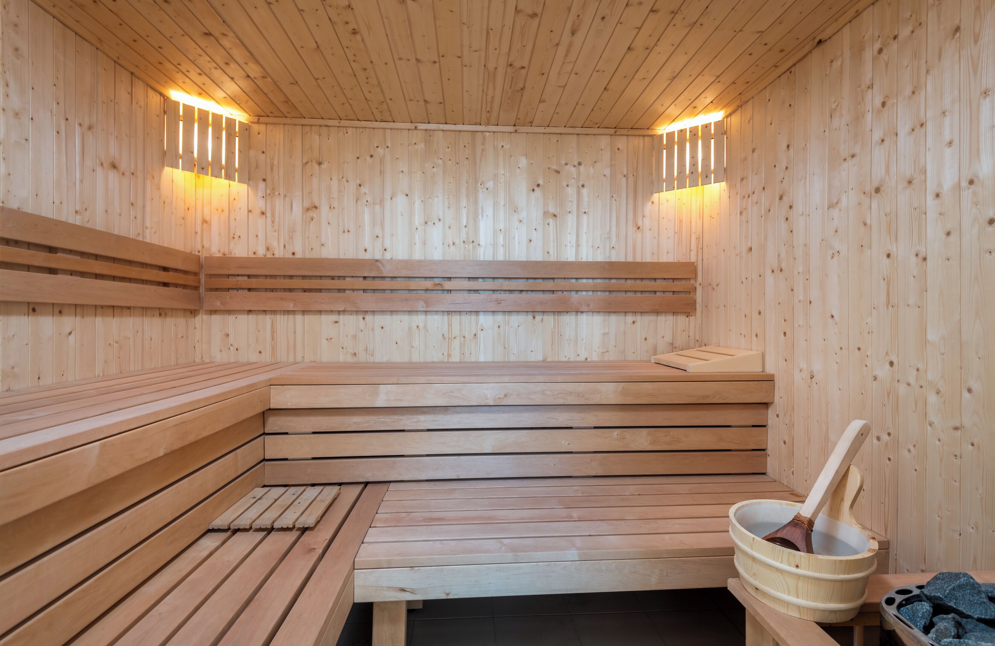 Eine Holzsauna mit Bänken und einem Holzeimer mit Schöpfkelle.