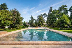 A rectangular swimming pool with clear water, surrounded by a paved deck and a grassy area with trees. - Hunguest Hotel Helios (Hévíz)