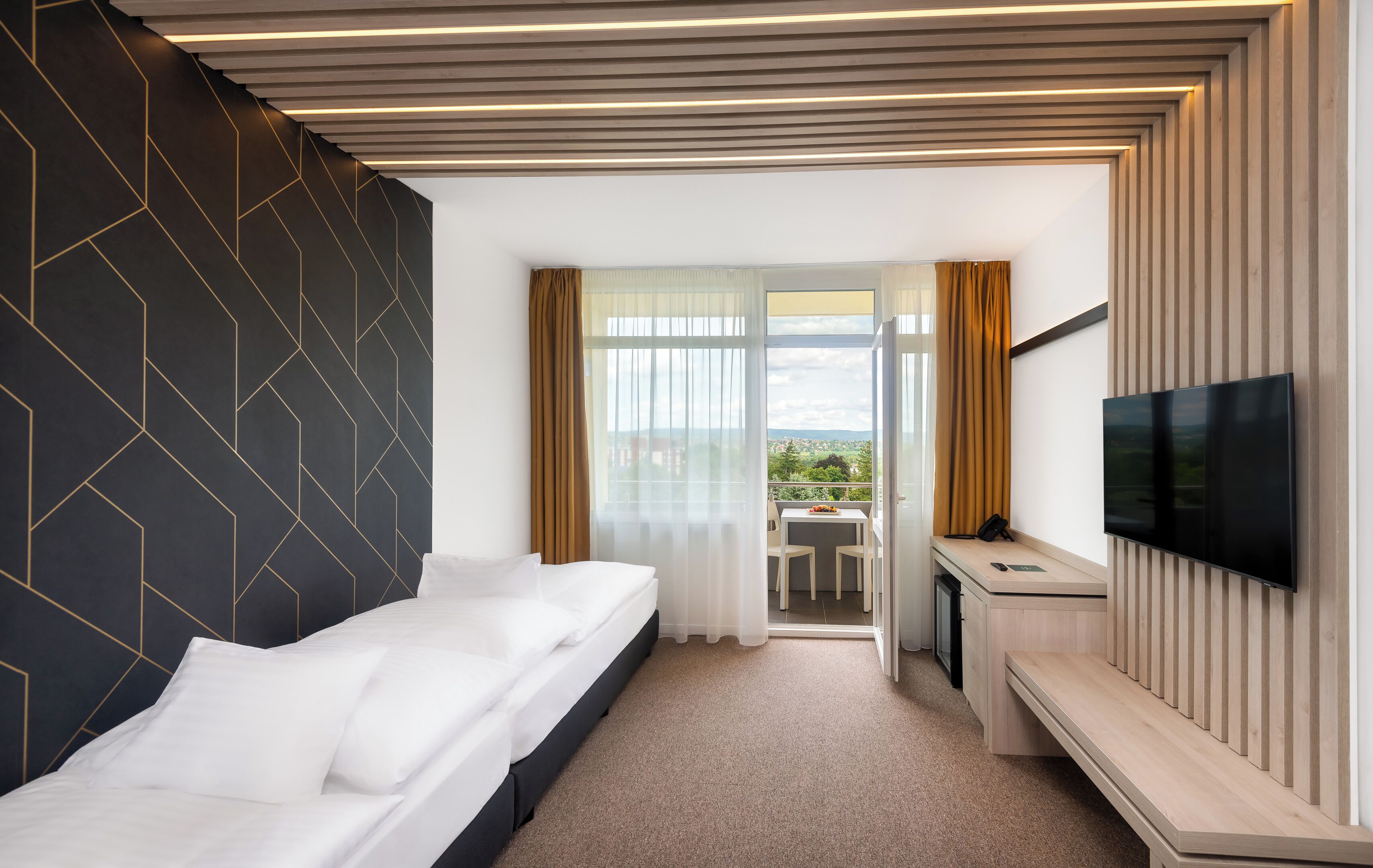 A modern hotel room with a bed, a desk, a TV, and a balcony with a view.