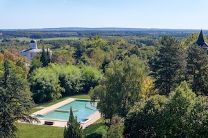 Una gran piscina rodeada de exuberante vegetación, con una iglesia y un edificio de techo puntiagudo al fondo.
