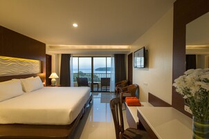 A hotel room with a large bed, a desk, a chair, a table, and a view of the sea.