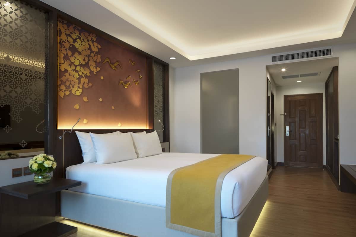 A modern hotel room with a large bed, a bedside table with a vase of flowers, and a decorative wall panel.
