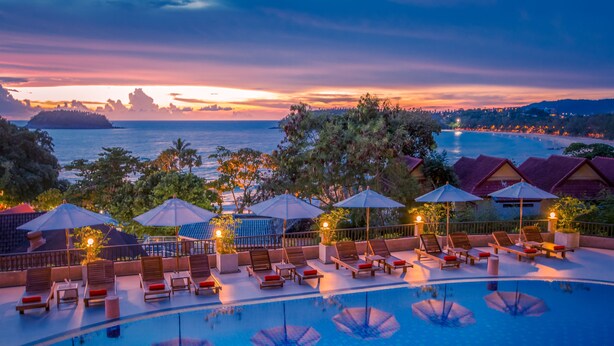 A poolside area with lounge chairs and umbrellas, overlooking a body of water and a sunset. - Chanalai Garden Resort, Kata Beach (Karon)