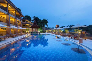A hotel pool area with lounge chairs and umbrellas, a reflection pool, and a multi-story building with balconies.