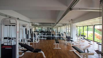 Uma academia com diversos aparelhos de exercício, bancos e um espelho grande na parede.