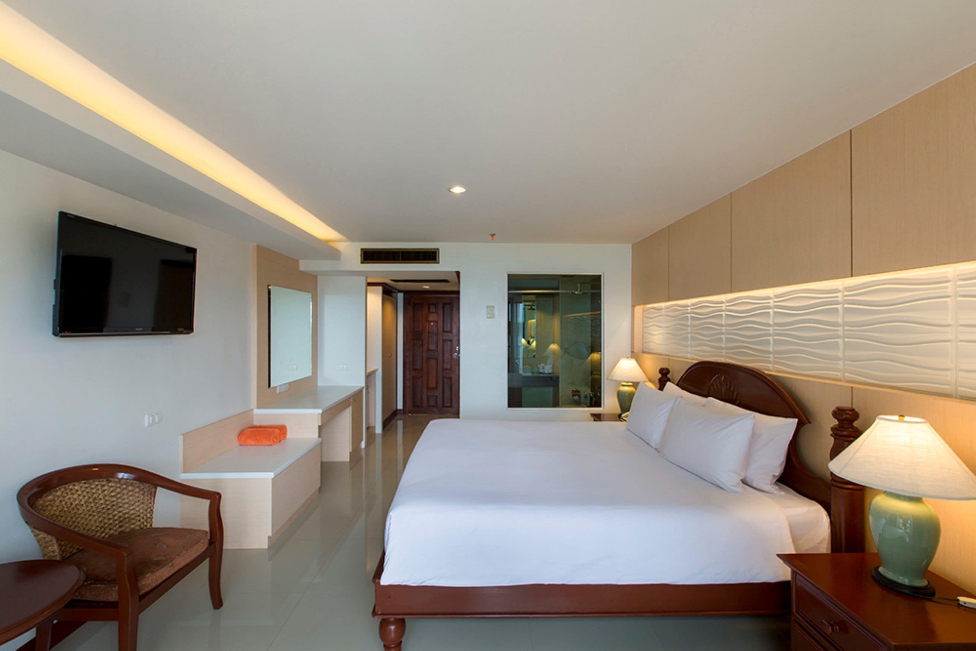 A hotel room with a bed, a desk, a chair, a TV, and a bathroom visible through an open door.
