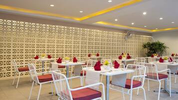 A restaurant with white metal chairs and tables, red cushions, and a decorative wall with a geometric pattern.