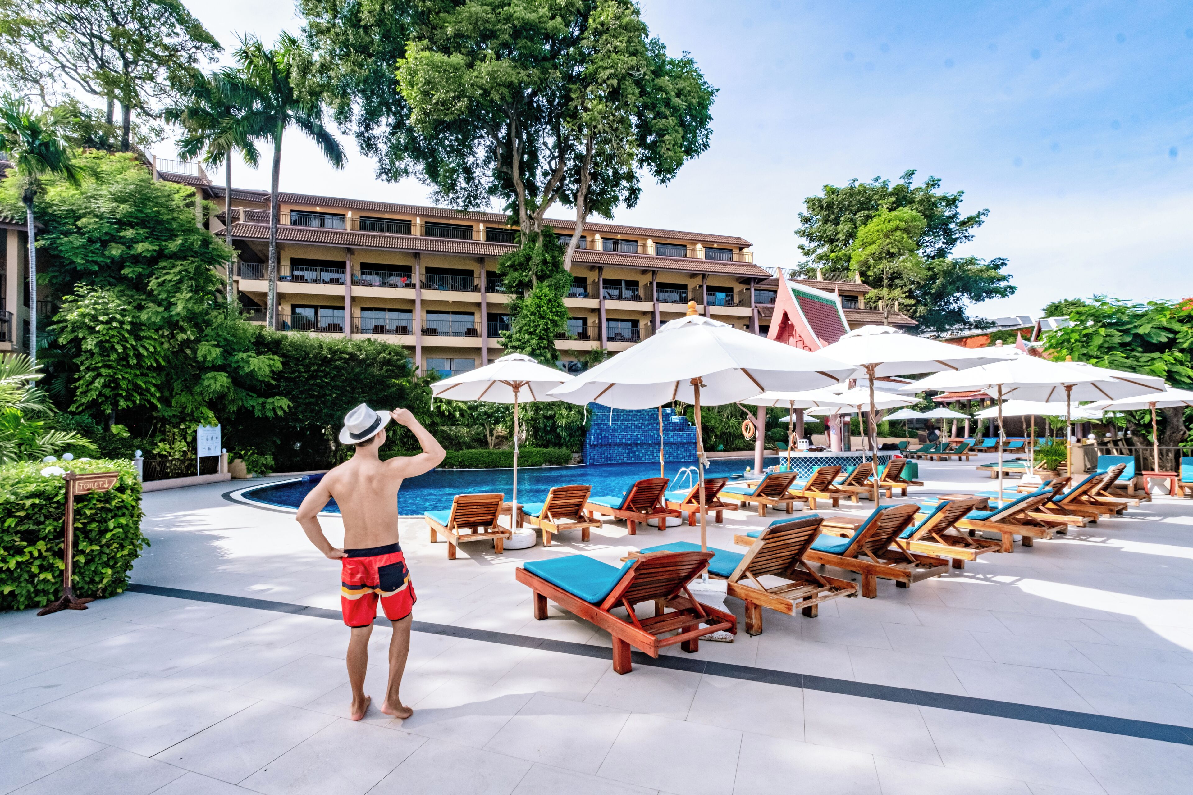 A poolside area with lounge chairs and umbrellas, a swimming pool, and a building with balconies.