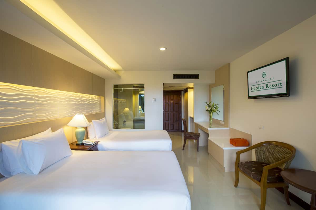 A hotel room with two beds, a sitting area with a chair and table, and a sign indicating it's Garden Resort.