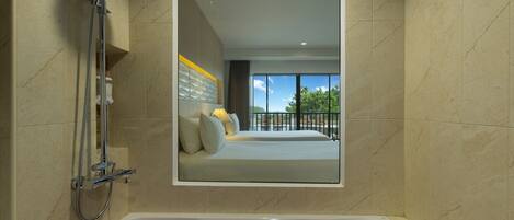 Ein modernes Badezimmer mit einer mit Rosenblättern gefüllten Badewanne, einer Duschkabine und einem großen Spiegel, der ein Schlafzimmer mit Balkon reflektiert.