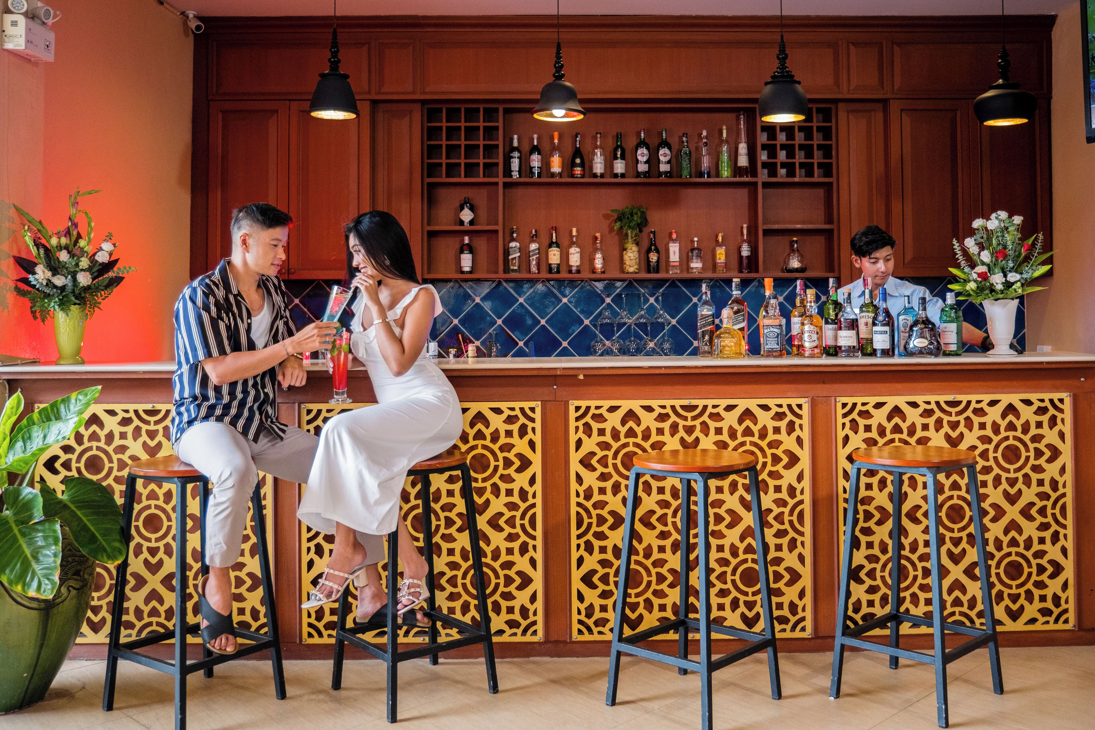A bar area with wooden cabinets, hanging lights, and stools.