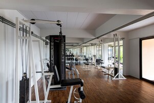 Un gimnasio con varios equipos de ejercicio, amplias ventanas y suelo de madera.