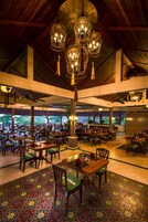 A spacious indoor dining area with multiple tables and chairs, ceiling fans, and hanging light fixtures.