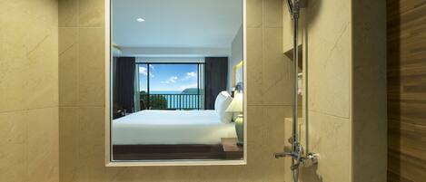 A modern bathroom with a large mirror reflecting a bedroom, a bathtub filled with rose petals, and a shower area.