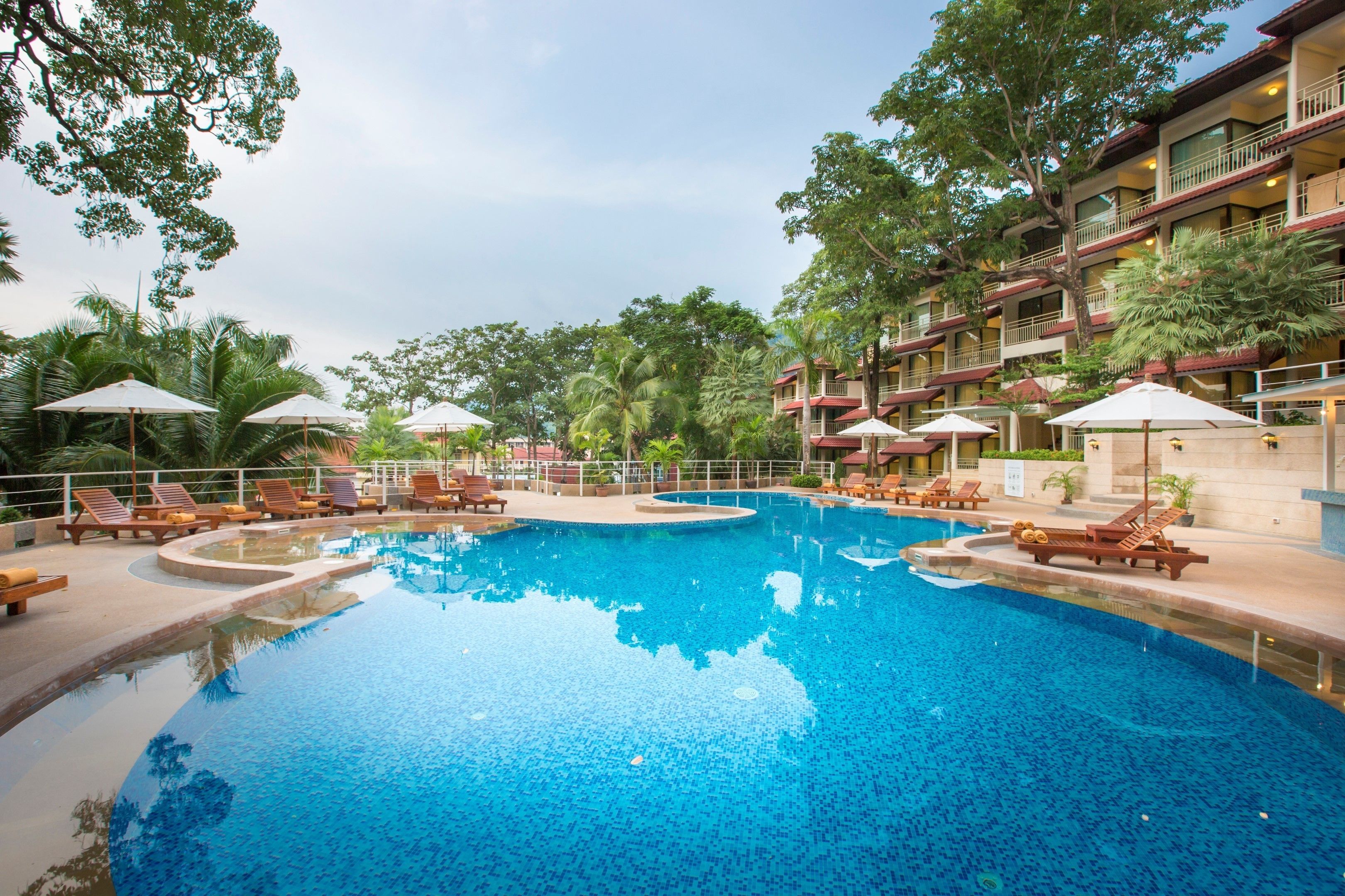 A swimming pool with lounge chairs and umbrellas, surrounded by a multi-story building with balconies.