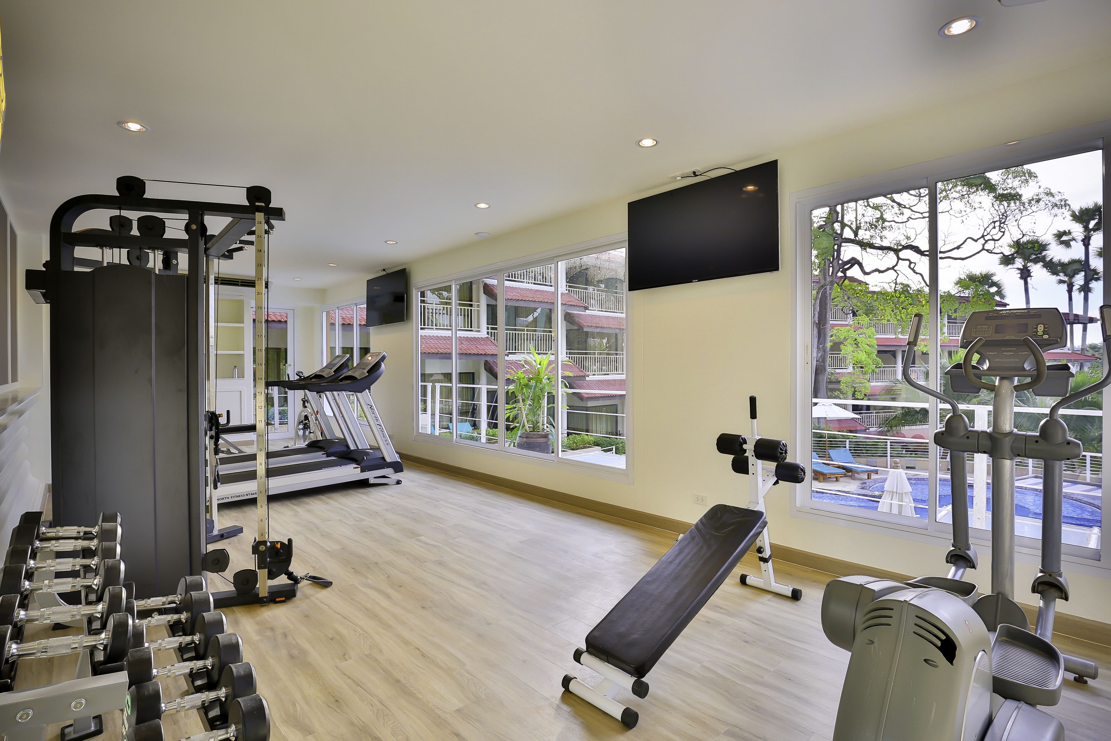A gym with exercise equipment, a treadmill, and large windows offering a view of buildings and trees.