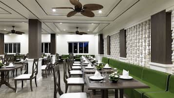 A restaurant with a modern interior, featuring green cushioned seating, wooden tables, and ceiling fans.