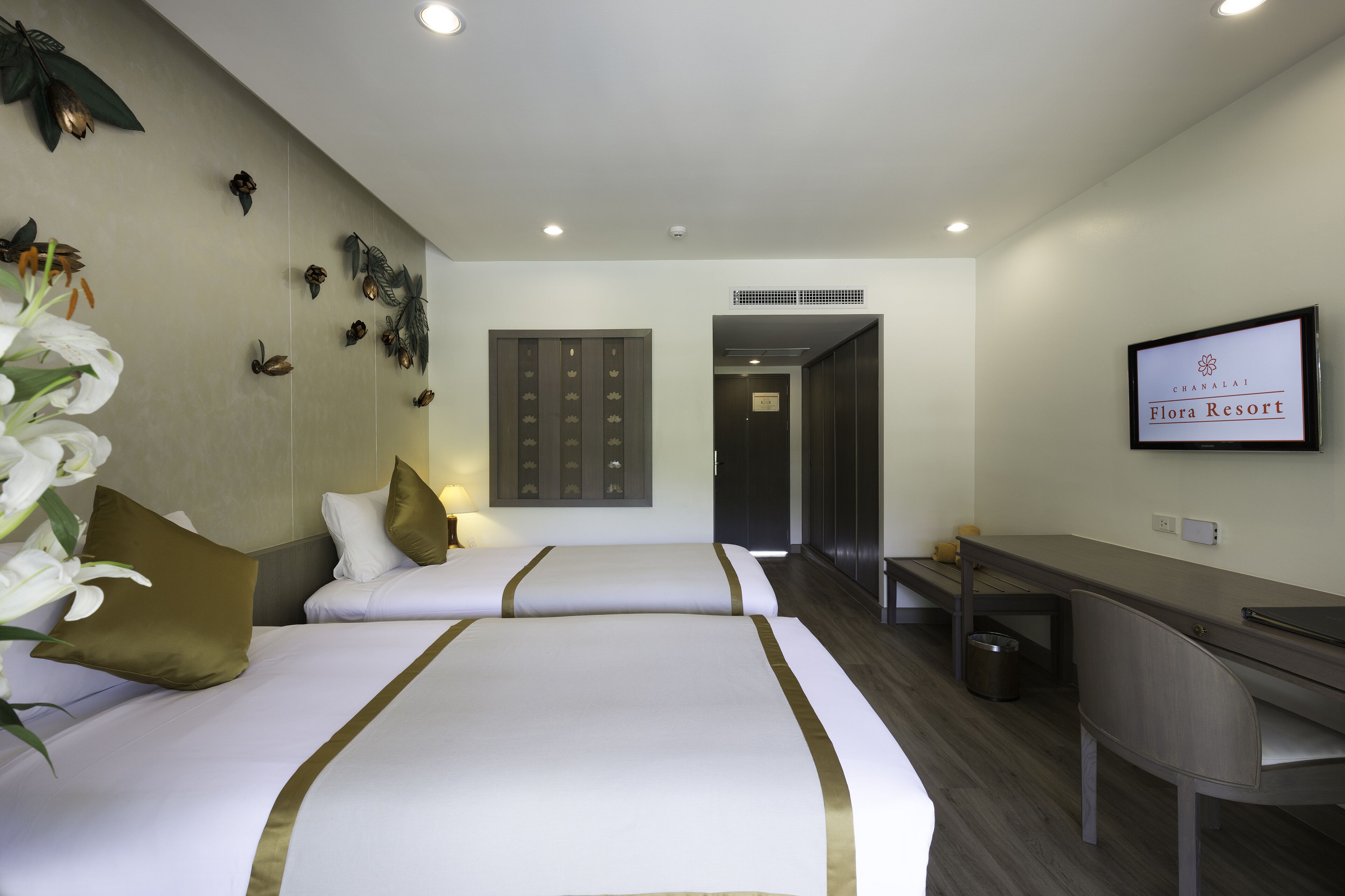 A hotel room with two beds, a desk, and a television displaying the hotel name.