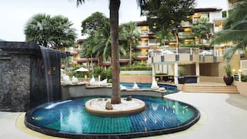 A resort pool with a circular design, palm trees, and a waterfall feature.