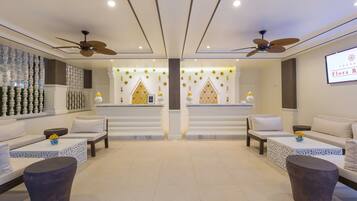 A modern hotel lobby with two seating areas, each with a sofa and a coffee table, and a central decorative wall with geometric patterns.