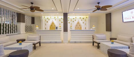 Un moderno vestíbulo de hotel con dos zonas de estar, cada una con un sofá y una mesa de centro, y una pared decorativa central con patrones geométricos.