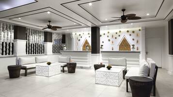 Un espace détente moderne avec des canapés blancs, une table basse et un mur décoratif orné de motifs géométriques.