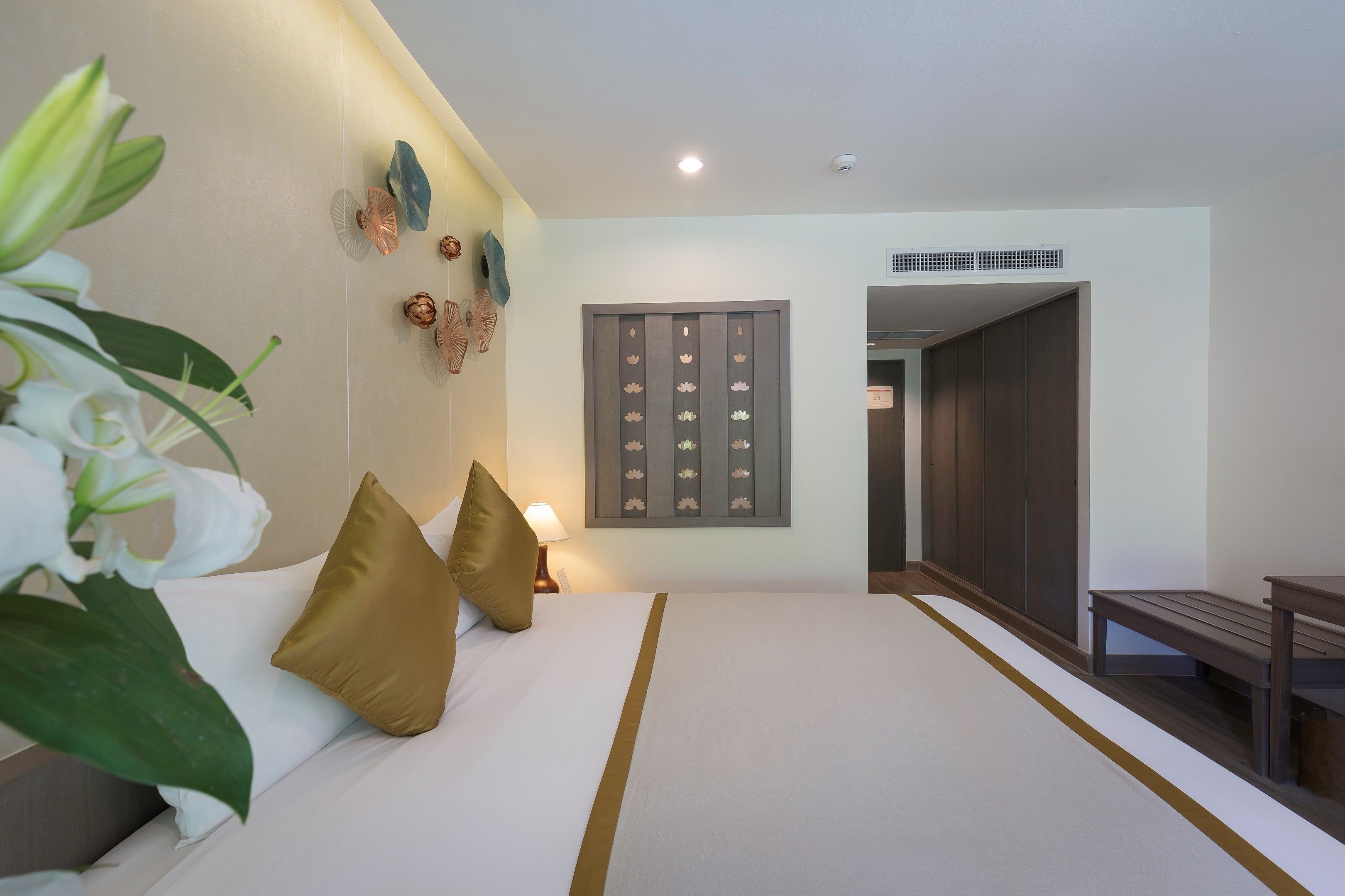 A hotel room with a large bed, a bedside table, a lamp, and a wall-mounted decorative panel.