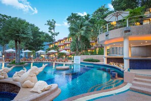 Un hotel con piscina que presenta esculturas decorativas, sillones de descanso y un edificio de varios niveles con balcones.