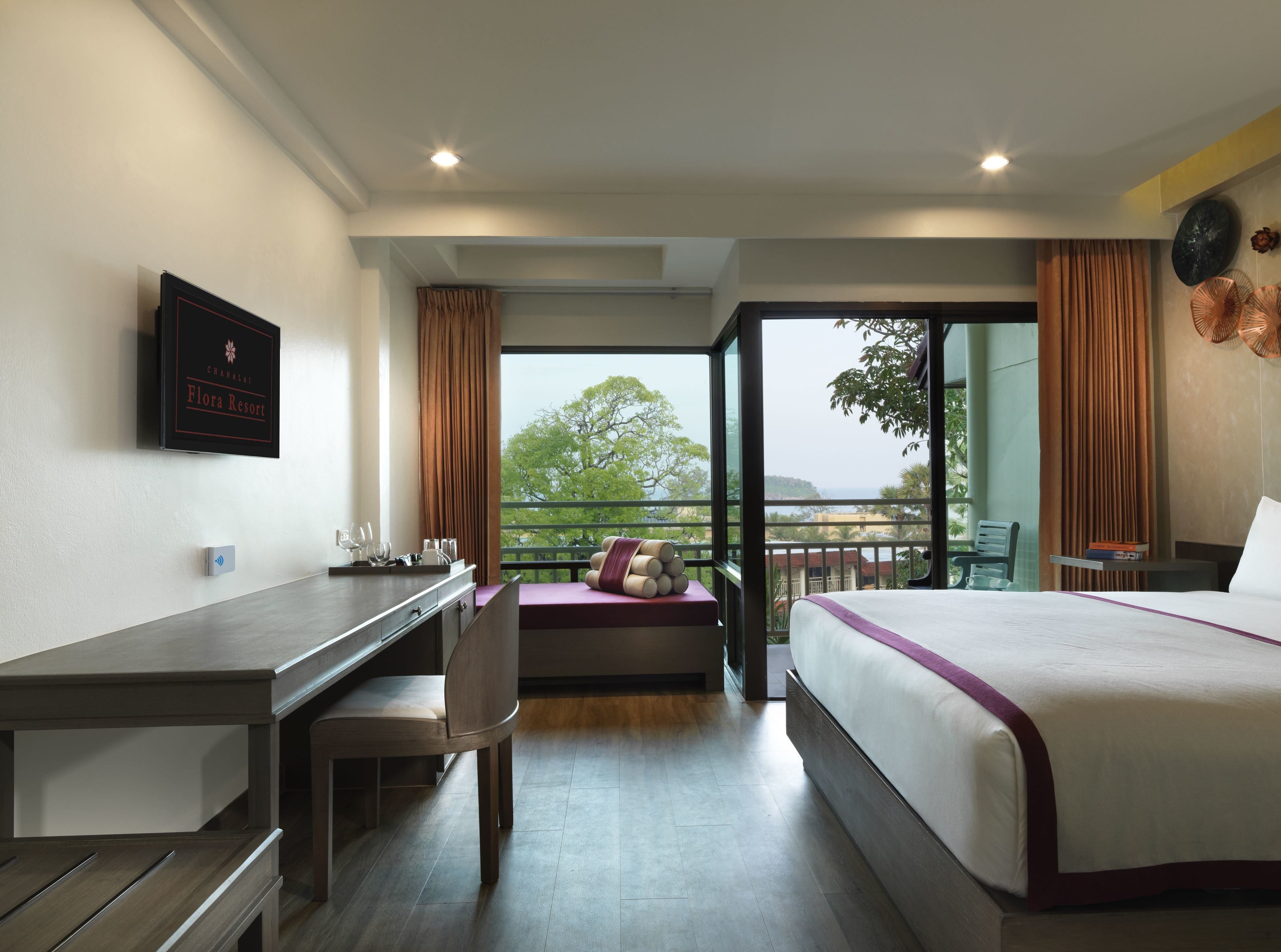 A hotel room with a bed, desk, chair, and a balcony with a view.