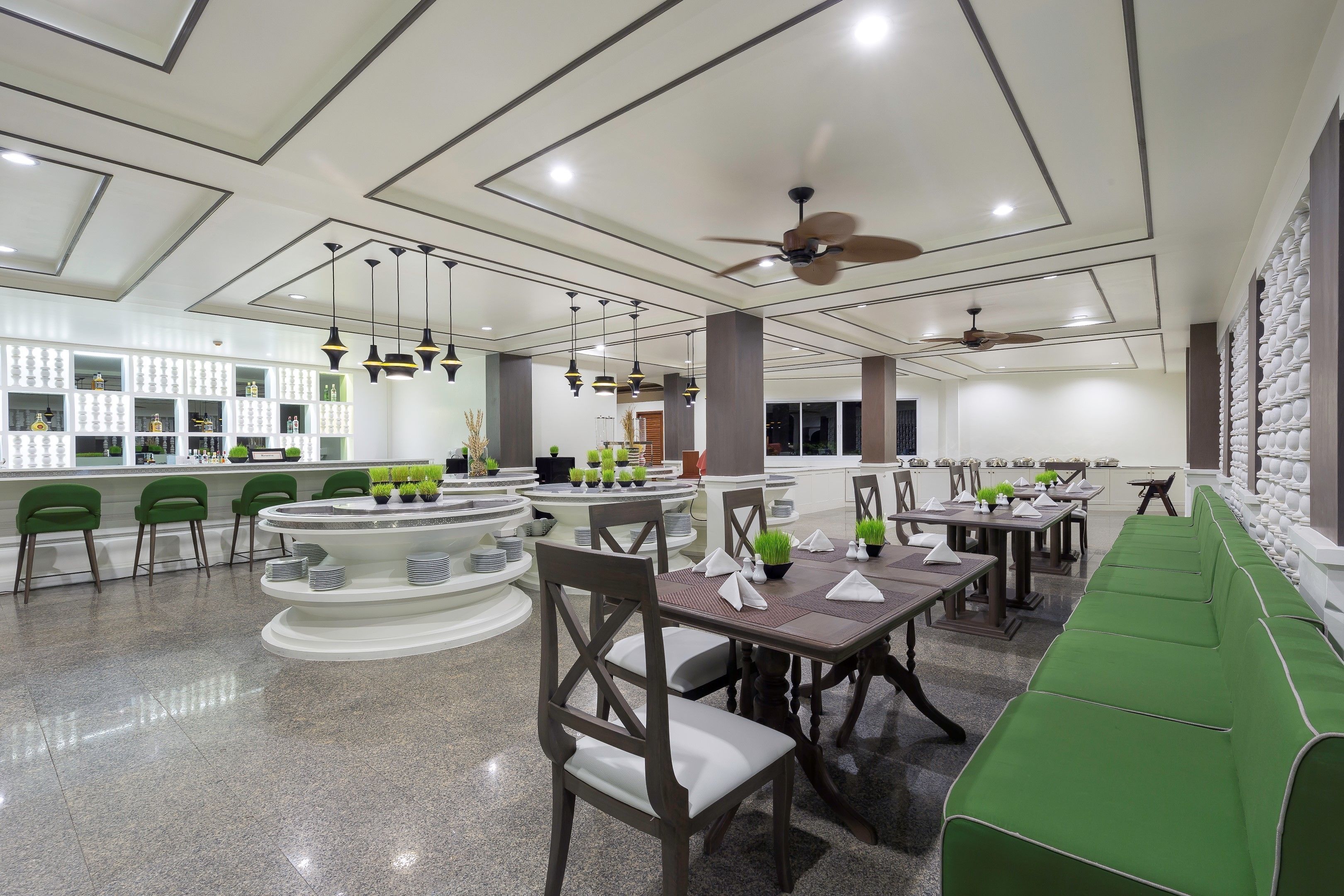 A modern restaurant with a central bar, green seating, and ceiling fans.