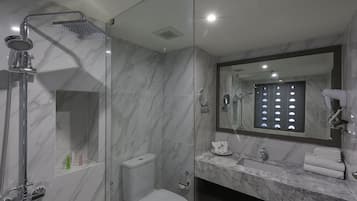 Un baño moderno con ducha de vidrio, inodoro, lavamanos con encimera de mármol y un espejo grande sobre el lavamanos.