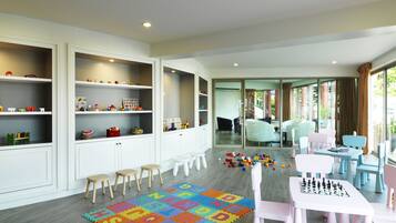A spacious children's playroom with white cabinets, colorful alphabet foam mats, and a chess table.