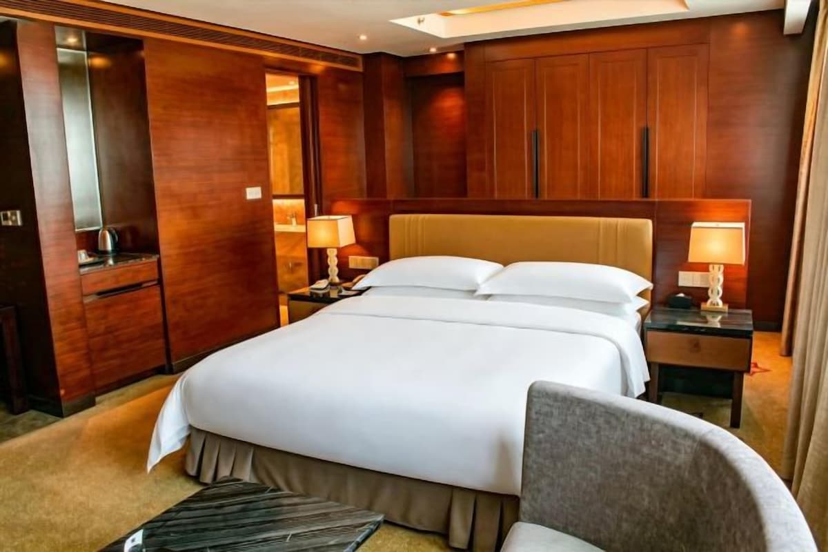 Ein Hotelzimmer mit einem großen Bett, einem hölzernen Kopfteil, zwei Nachttischen mit Lampen und einem Sessel.