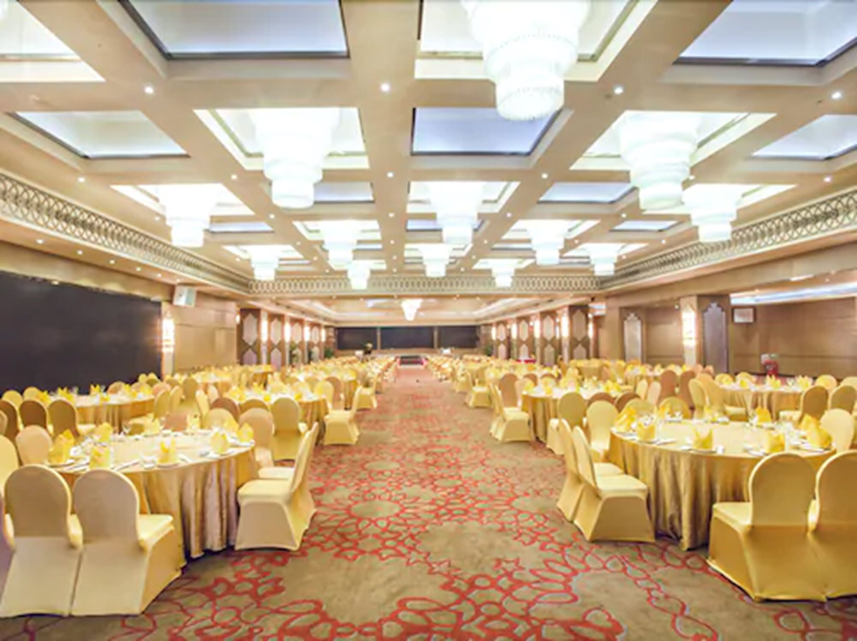 A banquet hall with round tables and chairs, a patterned carpet, and a high ceiling with skylights.