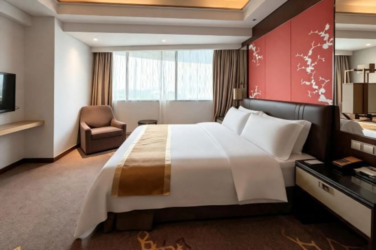 A hotel room with a large bed, a chair, a television, and a desk with a lamp.