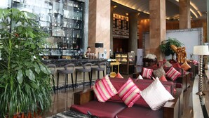 A modern lobby with a bar area, seating with striped cushions, and a large potted plant. - Cinese Hotel Dongguan (Dongguan)